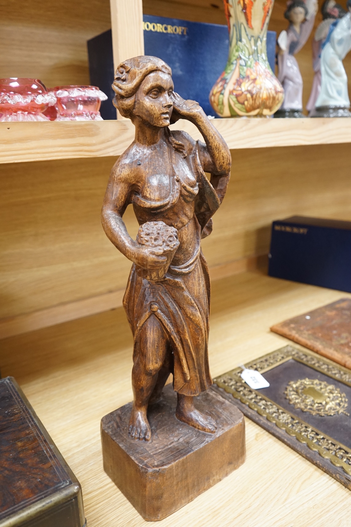 A carved walnut figure of a girl holding a basket of flowers, 54cm high